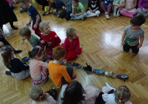 Dzieci siedzą przed ustawionymi w rzędzie butami.